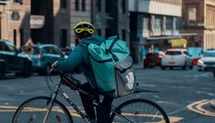 a man riding a bike down the street with a backpack on it's back