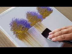 a person is painting with purple and yellow paint on a white canvas while holding a brush