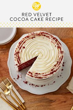 a red velvet cake with white frosting on a wooden table next to gold forks