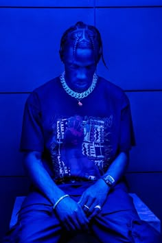 a man sitting down in front of a blue wall with his hands on his knees