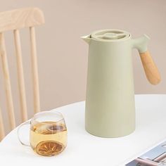 a pitcher sitting on top of a white table next to a glass filled with liquid