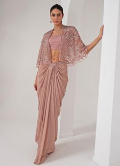 Elevate your style with the stunning Pastel Pink Draped Skirt with Embellished Cape, that effortlessly blends tradition with contemporary elegance. The pink cape features a sophisticated kimono sleeve , adorned with intricate florence embroidery using sequins, crystal tassels, cutdana, and bead highlights, adding a touch of opulence. Paired perfectly with a sequin jaal embellished blouse, it offers a dazzling appeal, making you the center of attention. Completed with a draped skirt, designed for a flattering silhouette, exudes grace and charm, ensuring comfort and sophistication in every movement. Ideal for, this ensemble is a timeless addition to your wardrobe, exuding both modernity and tradition in every detail. Composition : Cape - Organza ,Skirt - Platinoir Crepe Care: Dry Clean Only Elegant Draped Pink Sets, Elegant Pink Draped Sets, Elegant Fitted Pre-draped Saree With Cape Sleeves, Elegant Embroidered Pre-draped Saree For Evening, Elegant Pink Pre-draped Saree For Formal Occasions, Traditional Drape Pre-draped Saree, Traditional Pre-draped Saree For Occasion Wear, Embellished Fitted Pre-draped Saree With Cape Sleeves, Elegant Pre-draped Festive Saree