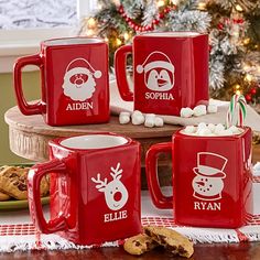 four red mugs with santa's faces on them sitting in front of a christmas tree