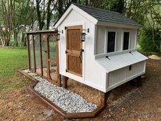 a chicken coop in the middle of a field with gravel around it and a wooden door