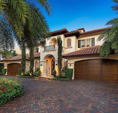 a large house with palm trees in front of it and a driveway leading to the garage