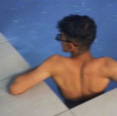 a man with no shirt sitting in a swimming pool looking at something off to the side