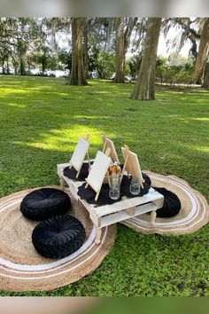 three chairs and two tables in the grass with black cushions on them, near some trees