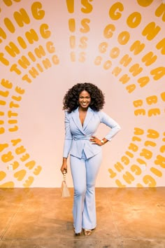 a woman standing in front of a wall with words on it and wearing a blue suit