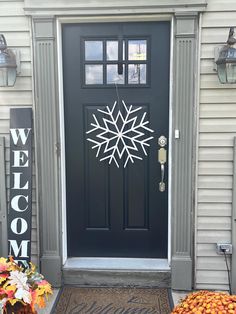 a black front door with a white snowflake on it and welcome sign next to it