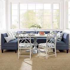 a living room with blue couches and white chairs around a small table in front of two windows