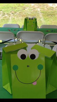 green paper bags with faces on them are sitting on a table in front of chairs