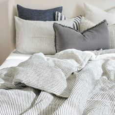 an unmade bed with striped sheets and pillows