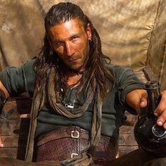 a man with dreadlocks sitting on a chair holding a teapot in his hand