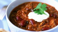 a white bowl filled with chili and sour cream on top of a blue table cloth