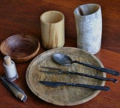 an assortment of kitchen utensils and spoons on a wooden plate with two cups