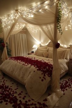 a bed with rose petals on the floor and lights strung up above it, in a bedroom decorated for valentine's day