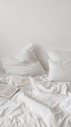 an unmade bed with white sheets, pillows and a book on the end table