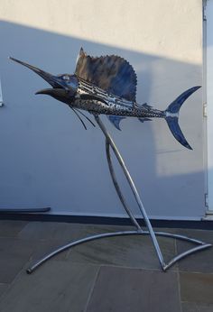 a metal sculpture of a sailfish on a stone floor in front of a white wall