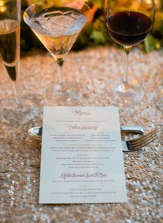 two glasses of wine are sitting on a table next to a menu and silverware