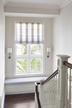 a white staircase leading up to a window with blinds on the windowsill and a bench in front of it