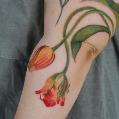 a close up of a person's arm with tattoos on it, including flowers and leaves