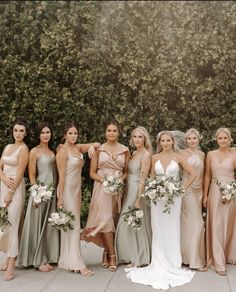 a group of women standing next to each other in front of a wall with greenery