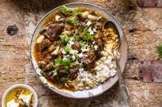 two bowls filled with stew and rice on top of a wooden table next to other dishes