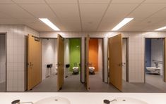 three sinks in a public restroom with multiple doors open to reveal two toilets and one urinal