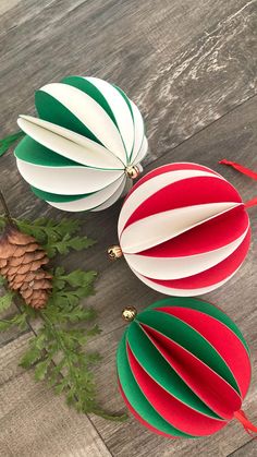 three paper christmas ornaments sitting on top of a wooden table next to a pine cone