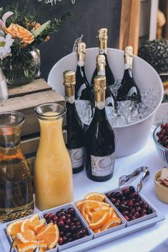 bottles of champagne, orange slices and cranberries are on a table with flowers