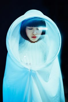 a woman in a white sweater is looking through a plastic covering over her head and holding a cell phone to her ear