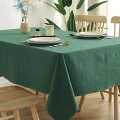 a green table cloth with white plates and silverware on it in front of a potted plant