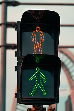 a traffic light with two green pedestrian lights on it's sides and an orange pedestrian crossing signal in the background