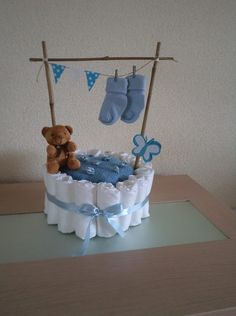 a teddy bear sitting on top of a diaper cake with socks hanging from the clothesline