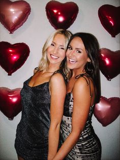 two beautiful women standing next to each other in front of heart shaped wallpapers