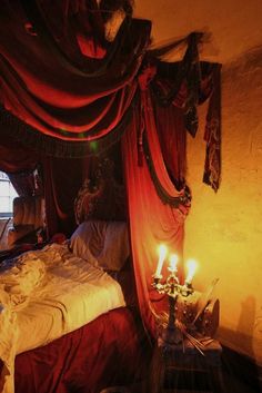 a bed with red drapes and two candles on it