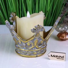 a lit candle sits in a crown shaped container on a table next to some green grass