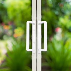 an open door with two white handles in front of green plants and trees behind it