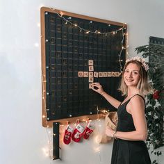 a woman is playing scrabble on a blackboard with christmas lights around her