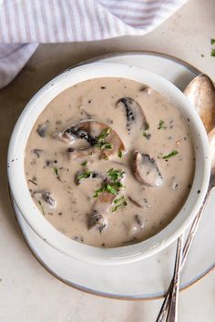 a white bowl filled with mushroom soup on top of a plate next to spoons