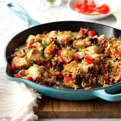 a skillet filled with chicken and rice on top of a wooden cutting board