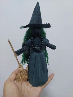 a hand holding a doll with green hair and a black hat on it's head