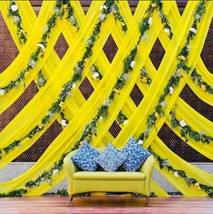 a couch sitting in front of a yellow curtain with flowers on it and a blue pillow