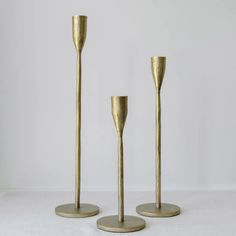 three gold colored candlesticks sitting on top of a white table next to each other