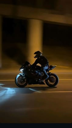 a man riding on the back of a motorcycle down a street at night with its lights on