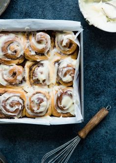 a box filled with cinnamon rolls on top of a blue counter next to other baking utensils