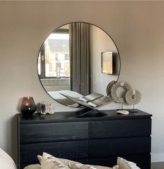 a black dresser with a round mirror above it