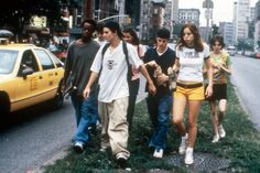 a group of young people walking down a street next to a yellow taxi and tall buildings