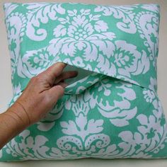 a hand is holding the edge of a green and white pillow