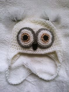 a crocheted owl hat with big eyes on top of a white blanket,